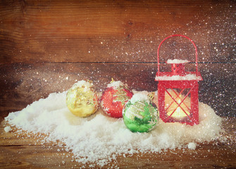 christmas background with red lantern, bauble and snow over wooden background. glitter overlay

