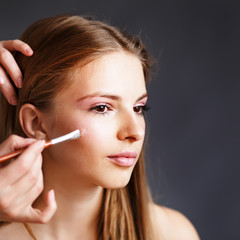 Young blonde girl applying make-up by make-up artist.