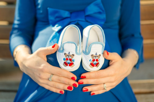 Pregnant woman holding baby sneakers on her belly