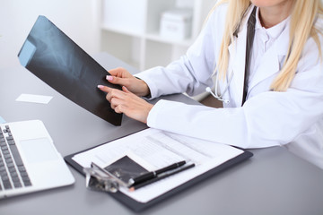 Close up of female doctor holding x-ray or roentgen image, sitting at the table