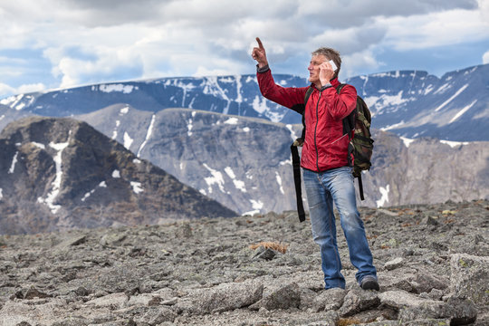 Mature Caucasian hiker a man shows to the mountain top, talking on a cell phone