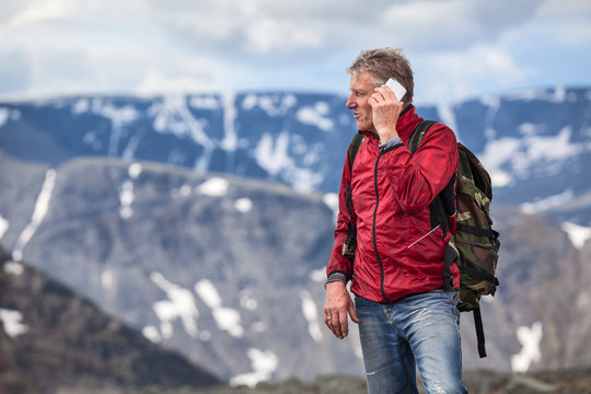 Mature Caucasian hiker talking on mobile phone on high of mountains, copy space