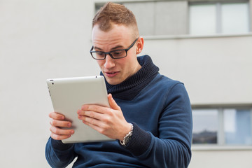 Stylish guy connected on internet with tablet in town. He is surprised.