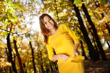 Young woman in the yellow dress with autumn leaves in hand and fall yellow maple garden background