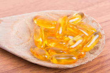 Cod liver oil omega 3 gel capsules on spoon wood