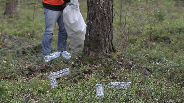 Man with bag picking up used plastic bottles in forest

