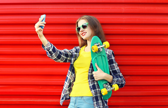 Pretty cool young woman in sunglasses with skateboard taking pic