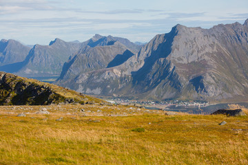 Fototapeta premium Beautiful Vibrant Norwegian Mountain Landscape from Ryten peak - famous mountain in Lofoten Islands, Moskenes municipality, Nordland with a view of Kvalvika beach, with hiking tourists and blue sky 