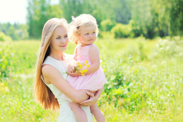 Mother holding on hands child with flowers in summer day