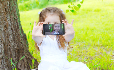 Child making self portrait on smartphone in summer park, screen