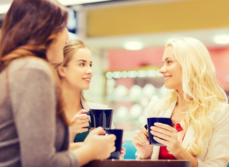 smiling young women with cups in mall or cafe