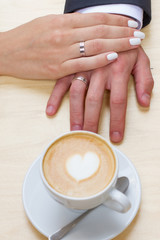 Women's and men's hands with wedding rings with cup of coffee