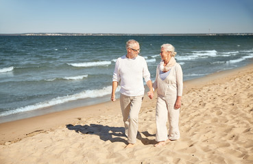 happy senior couple walking along summer beach