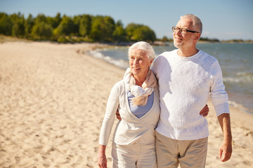 happy senior couple walking along summer beach