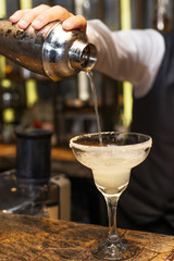 Barman at work, preparing cocktails. Pouring margarita to cocktail glass. concept about service and beverages.