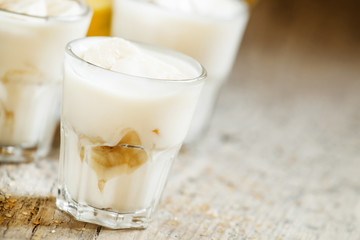 Fresh homemade banana yogurt in glass on old wooden table, selec