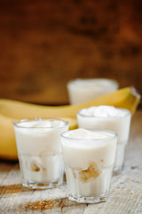 Fresh homemade banana yogurt in glass on old wooden table, selec