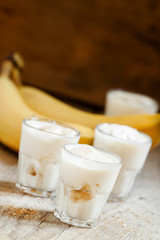 Fresh homemade banana yogurt in glass on old wooden table, selec