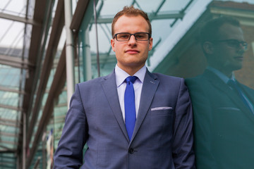 Portrait of young businessman standing in front of office block.