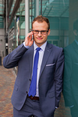 Caucasian businessman outside office using mobile phone on a office block background.