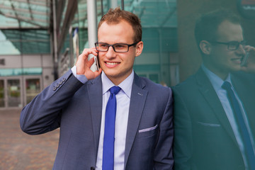 Caucasian businessman outside office using mobile phone on a office block background.