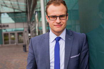 Fototapeta premium Portrait of young businessman standing in front of office block.