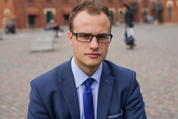 Portrait of young businessman standing in front of office block.