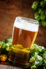 glass of foamy beer and hop cones on old wooden background, sele