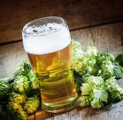 glass of foamy beer and hop cones on old wooden background, sele