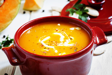 Pumpkin soup in a red bowl on white wooden background, selective