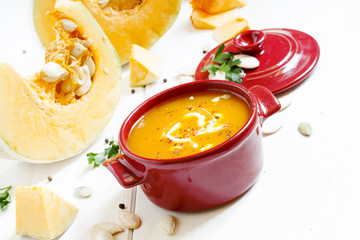 Pumpkin soup in a red bowl on white wooden background, selective