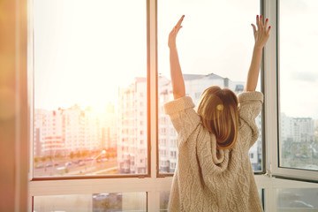 Woman near window raising hands facing the sunrise at morning - 92374605
