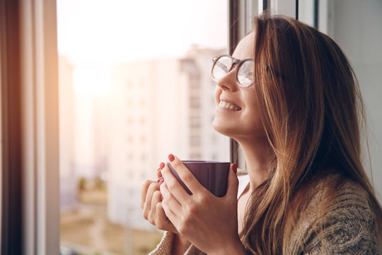 cheerful girl drinking coffee or tea in morning sunlight