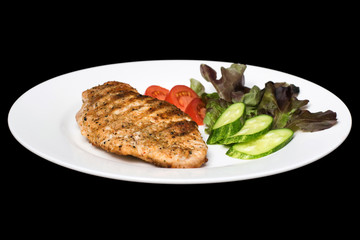 Photo of a chicken stake on a white plate with a cucumber, tomat