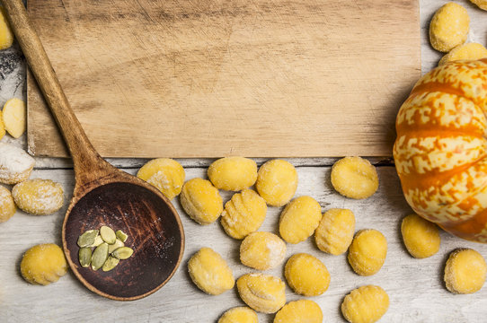 pumpkin gnocchi with pumpkin,  wooden spoon,almonds , flour on wooden cutting board, on wooden rustic background top view