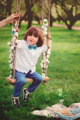 cute toddler boy relaxing on swing in spring garden on picnic