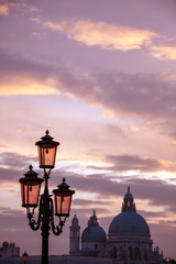 Italy Venice island city at sunset view over the gondola poles to Santa Maria della Salute cathedral over canal illuminated Murano glass lamps