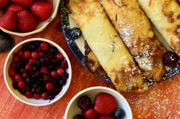 Yummy crepes with strawberries and huckleberries on wooden background