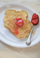 Macerated strawberries spooned over French toast on a white platter