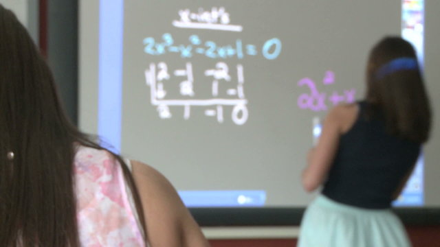 Student working on math problem on board in front of classroom