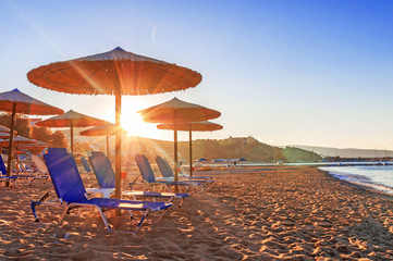 Two blue sunbed, straw umbrella on beautiful beach background with burning sun