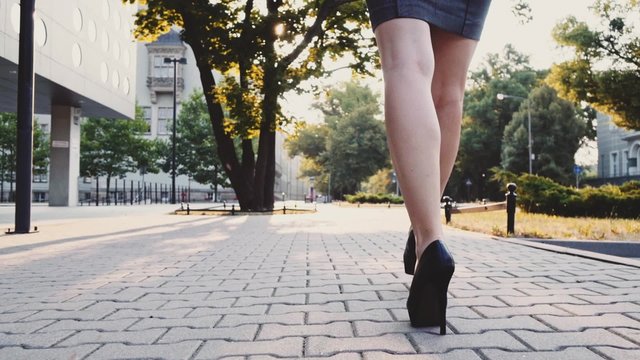 Attractive business woman walking in the city, drinking coffee and talking on a phone in the morning. Steadicam stabilized shot in Slow motion. Lens flare. Sexy woman legs in black high-heeled shoes.