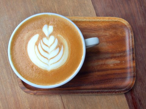 flat white coffee with latte art, this pattern is commonly called "tulip" on wooden saucer and table in cafe.