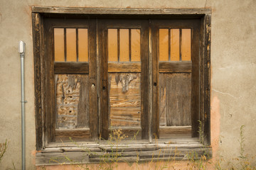 Three old brown doors, each with three orange windows, in tan plaster wall, Jackson, Wyoming.