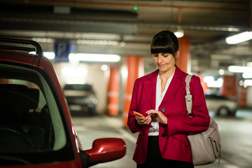 Senior business woman with phone at car
