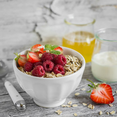 oatmeal with raspberries, strawberries and natural yoghurt in a bowl on a light wooden background