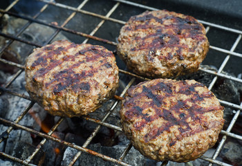 Burgers patties over flames on a grill.
