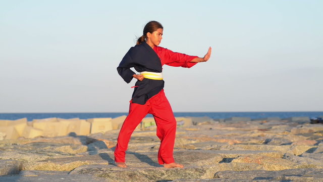 Beautiful girl practicing self defense on rocks near ocean