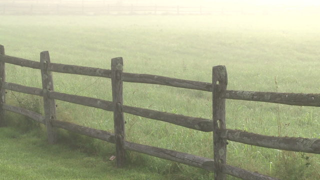 Looking over a split rail fence to  a foggy meadow