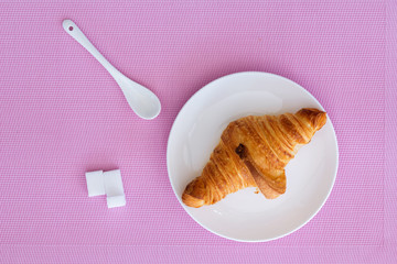one croissant on a white plate and white cup of Coffee on a pink background. top view. Buffet breakfast, a teaspoon of white, refined white sugar cubes
